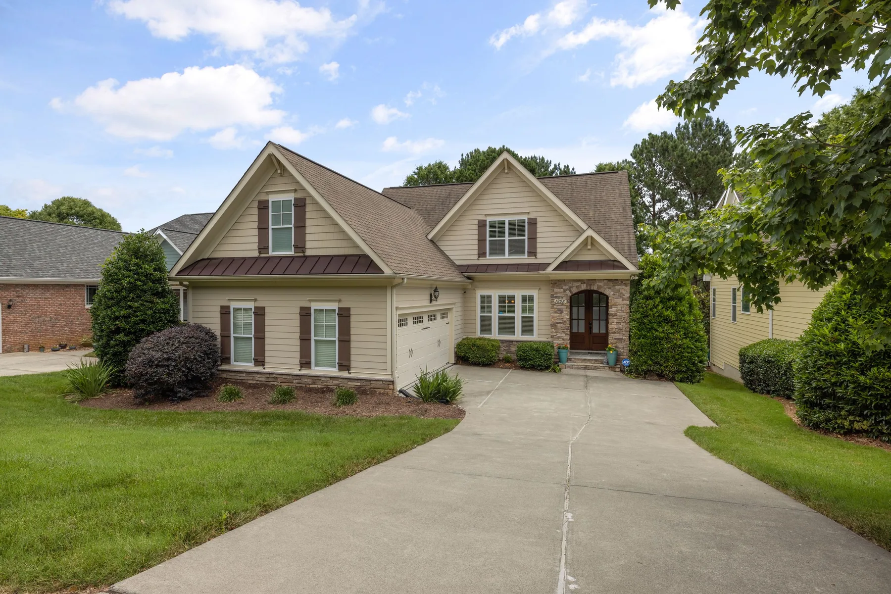 A finished detached house with dormers, a stone and siding facade, a double garage, a mown lawn and a concrete driveway.